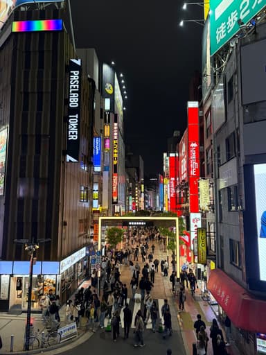 A crowded, neon-lit pedestrian street in Shinjuku, Tokyo at night.