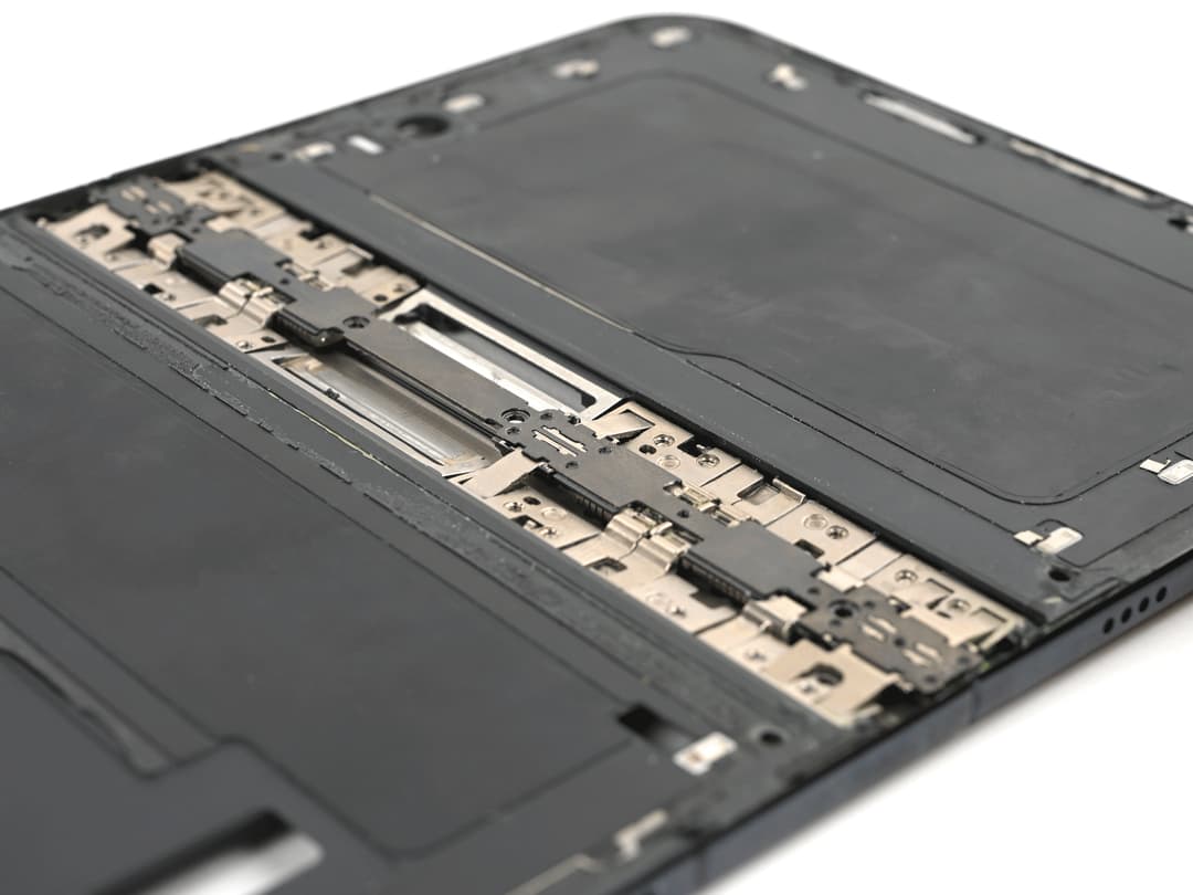 Close-up, at an angle, of an opened iPhone Duo with its inner screen removed, showing interlocking metal hinge links and plates running across the middle of the dark frame.