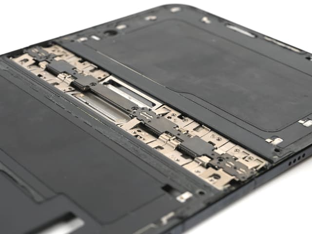 Close-up, at an angle, of an opened iPhone Duo with its inner screen removed, showing interlocking metal hinge links and plates running across the middle of the dark frame.
