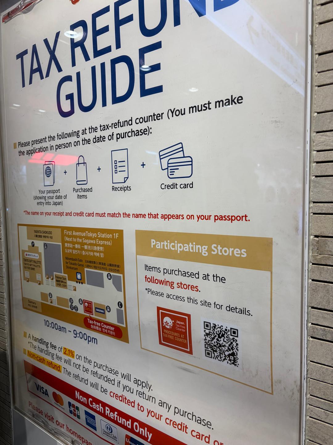 A wall sign titled "Tax Refund Guide" at a tax-free counter at Tokyo Station. It asks shoppers to bring their passport, purchased items, receipts and a credit card, shows a map of the counter on the first floor of First Avenue Tokyo Station, open 10am to 9pm, and says a handling fee of 2.1% on the purchase will apply, with non-cash refunds only.