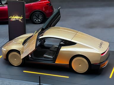 A gold two-door sports car with butterfly doors open is parked indoors, with a red SUV and a CyberTrak sign in the
