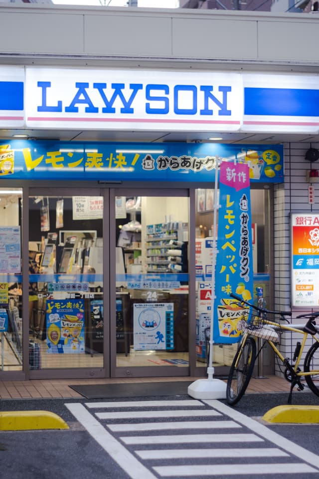A nighttime photo of the entrance to a Lawson convenience store in Fukuoka, Japan, showcasing its vibrant signage.